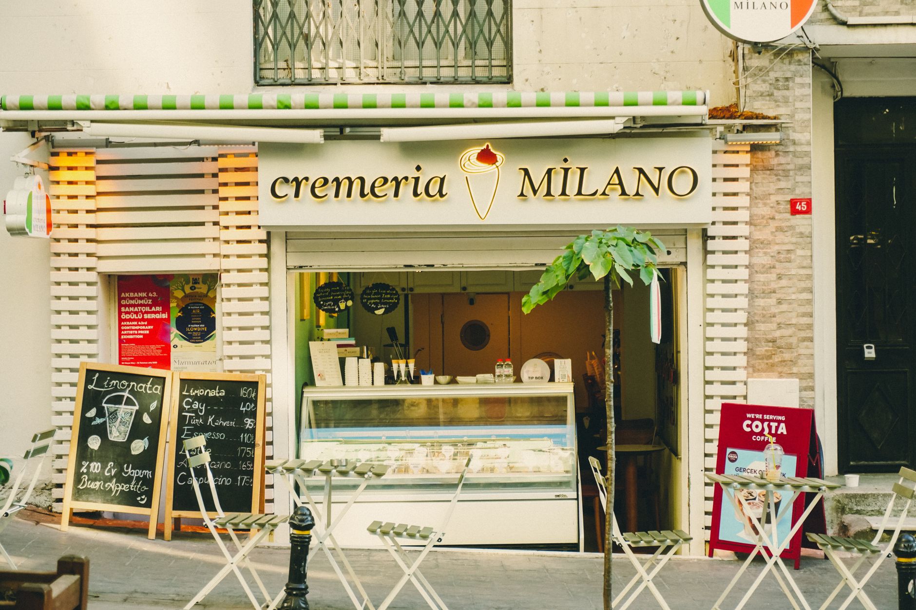 A cozy gelato shop named Cremeria Milano with outdoor seating in a sunny urban area.